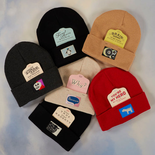 Six beanie hats in various colors, each with a unique patch design featuring different text and illustrations, arranged in a circle on a soft gradient background.