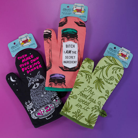 Three colorful oven mitts on a purple gradient background, each with bold, humorous text and unique illustrations, including a raccoon, bottles, and green leaves.