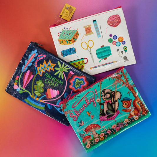 Three colorful zipper pouches on a vibrant gradient background; one with sewing supplies, one with “Random Crap” and flowers, and one with cartoon animals and the word “Skunky!” among mushrooms.