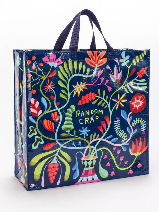 The Blue Q Random Crap Shopper is a reusable tote with a navy background, colorful abstract flowers and leaves, and "RANDOM CRAP" in the center. Sturdy black handles make it ideal for groceries or as a gym bag.