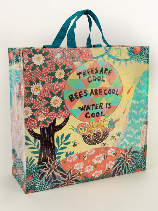 The Blue Q "Trees Are Cool. Bees Are Cool. Water Is Cool." Shopper is a colorful reusable bag with blue handles, featuring trees, flowers, bees, water, and cute creatures beside the slogan: TREES ARE COOL, BEES ARE COOL, WATER IS COOL.