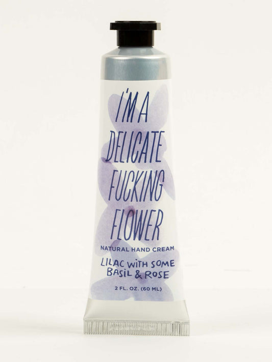 A 2 fl. oz. tube of Blue Q's "I'm a Delicate Fucking Flower" Natural Hand Cream—Lilac with Some Basil & Rose, enriched with shea butter and vitamin E—set against a plain background.
