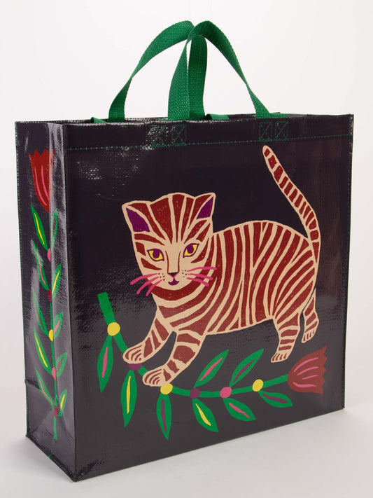 The Blue Q Tiger Kitten Shopper is a reusable shopping bag with sturdy green handles, featuring a vibrant striped cat amid green leaves and red tulips on a dark background.
