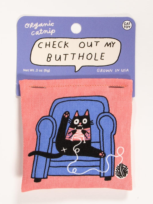 The Check Out My Butthole Catnip Toy by Blue Q features a cartoon black cat on a blue armchair with pink yarn and the phrase above. The package says organic catnip, grown in the USA, and encourages healthy play.