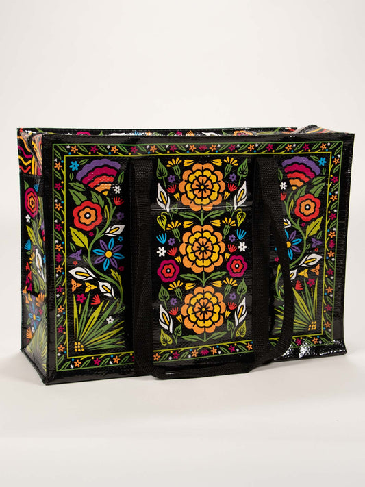 The Blue Q Flower Fest Shoulder Tote is a spacious, practical bag with black handles, featuring vibrant floral patterns and bright blooms set against a black background.