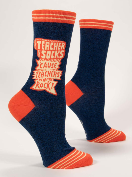 Blue Q Teacher Socks 'Cause Teachers Rock W-Crew Socks feature navy blue with orange accents and stripes, bold "Teacher Socks Cause Teachers Rock!" lettering, and are crafted from soft combed cotton with stretchy spandex for comfort.