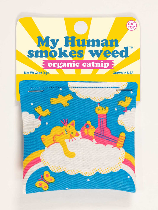 The Blue Q "My Human Smokes Weed Catnip Toy" is a colorful cotton pouch with organic, USA-grown catnip. The blue packaging shows yellow cats, clouds, and rainbows for healthy and fun play.