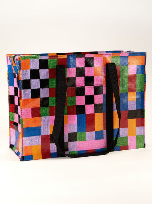 The Blue Q Color Cube Shoulder Tote is a rectangular bag with black handles, a zipper closure, and a vibrant patchwork of multicolored squares and rectangles, shown on a plain white background.