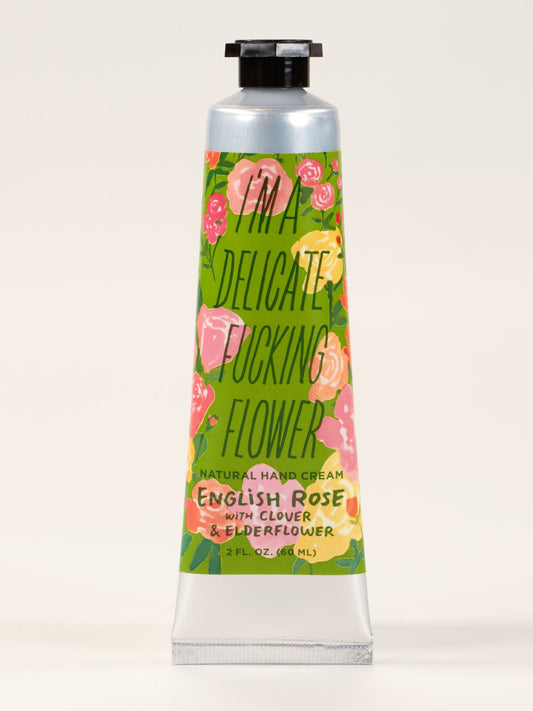 A metal tube of Blue Q's "I'm A Delicate Fucking Flower" Hand Cream—English Rose with clover, elderflower & shea butter. Decorated with colorful flowers. 2 fl. oz. (60 mL).