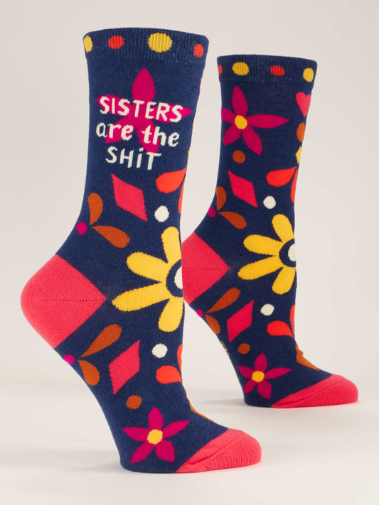 Blue Q Sisters Are The Shit W-Crew Socks feature navy blue cotton nylon with bold yellow, red, orange, and pink floral patterns and “SISTERS are the SHIT” in white and pink. Bright pink heels and toes add a standout touch.