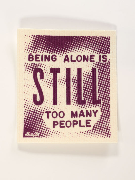 The Blue Q "Being Alone Is Still Too Many People" Swedish Dishcloth is a beige, compostable cloth with purple text in a bold, dotted design.
