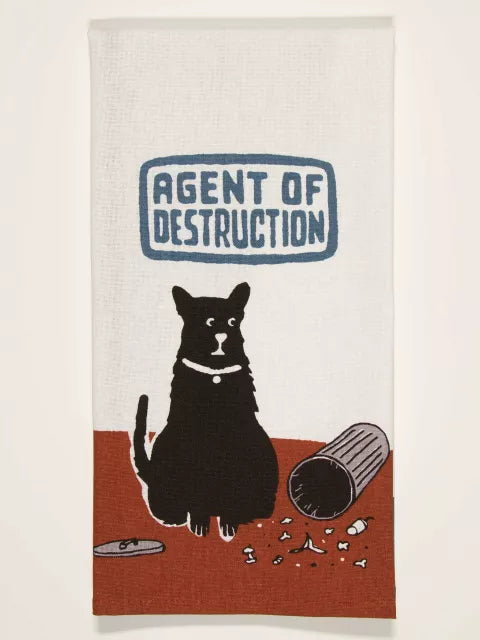 The Agent of Destruction Dish Towel by Blue Q features a black cat next to a toppled trash can with debris, watched by a forgiving dog. Bold text above the cat reads "AGENT OF DESTRUCTION.