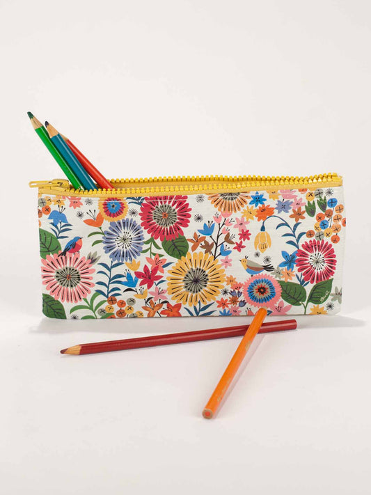 A Blue Q Flower Field Pencil Case with a yellow zipper holds three colored pencils; two others—orange and red—are in front of the case on a white surface.