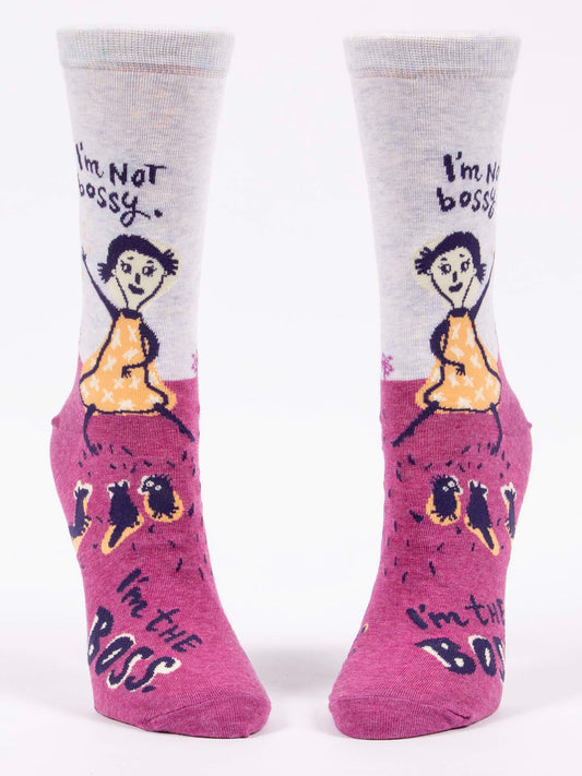 Blue Q’s "I'm Not Bossy. I'm The Boss" W-Crew Socks feature a cartoon woman in yellow with the phrase “I’m not bossy, I’m the boss” and small figures on a pink background—perfect for ladies who love fun combed cotton socks!.