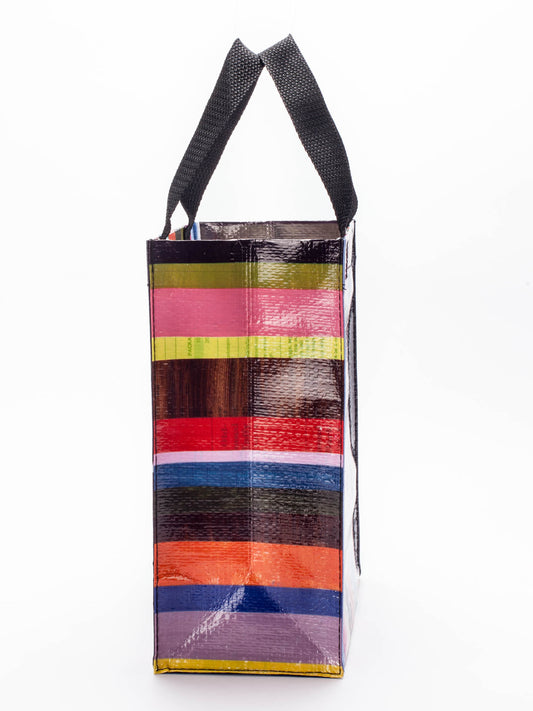 The Blue Q Doggy Handy Tote features sturdy black handles and a vibrant striped design in red, green, yellow, pink, blue, and orange. This rectangular reusable bag is perfect as a cute dog bag or stylish pet carrier. Stands upright on a white background.