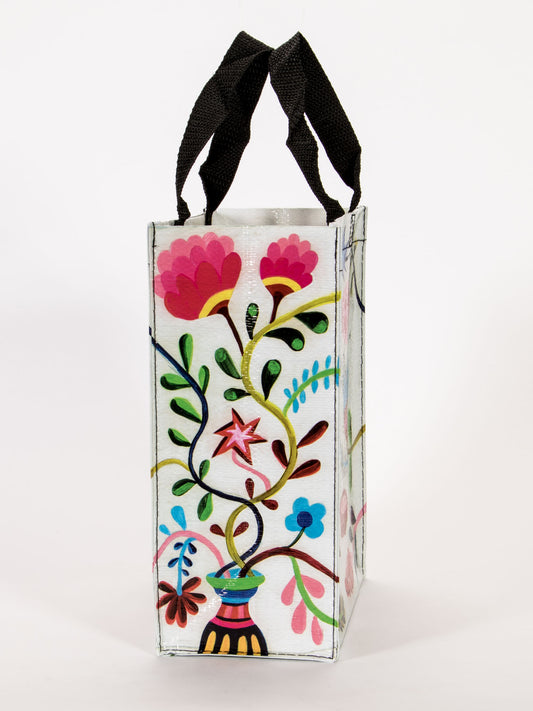 The Blue Q Chow Time Handy Tote features black handles and vibrant floral patterns—including pink flowers and a red star—on a white background, making it a stylish option for carrying your cat.