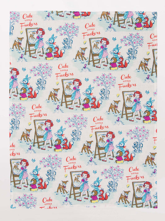 The Blue Q "Cute Little Fuckers" Dish Towel features vintage-style illustrations of children with animals, easels, and flowers, plus the phrase “Cute Little Fuckers” in playful red and yellow text.