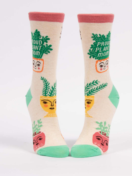 The Blue Q Proud Plant Mom W-Crew Socks are cream-colored combed cotton socks with green toes and heels, colorful Boston fern plant pot designs with smiling faces, and “Proud Plant Mom” on the upper part.