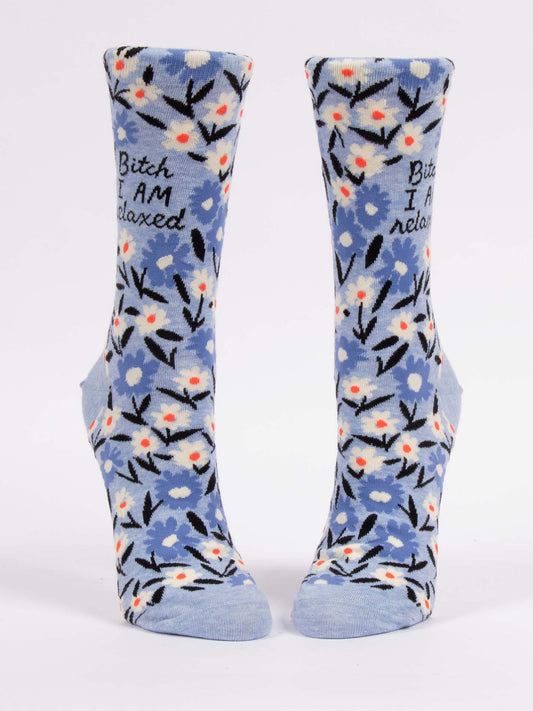 The Blue Q Bitch I AM Relaxed W-Crew Socks are blue with a white, black, and orange floral pattern and “Bitch I am relaxed” near the top. Shown upright on a white background.