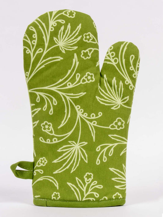 The Food Has Weed In It Oven Mitt by Blue Q is green with a subtle white floral and leaf design, includes a thumb section and hanging loop, and is shown on a plain white background.
