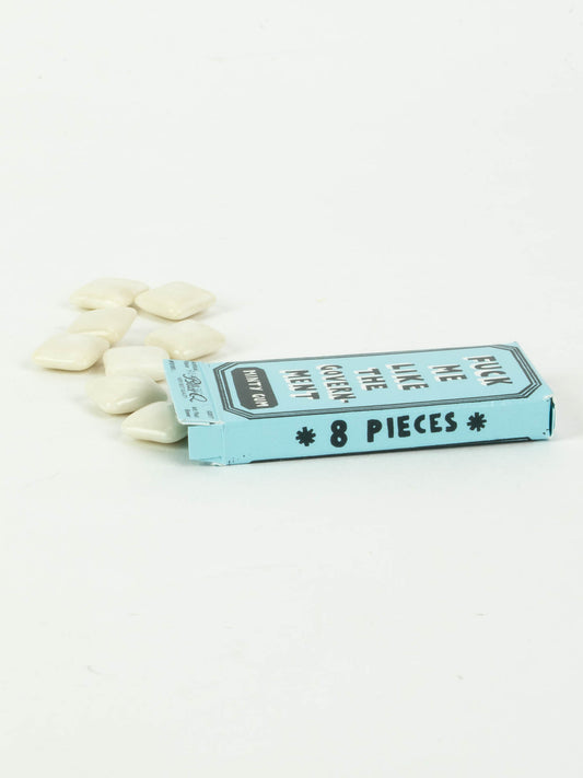 A light blue rectangular box labeled "Fuck Me Like The Government Gum" by Blue Q lies open on a white surface, with several white, diamond-shaped peppermint gum pieces spilling out beside it.