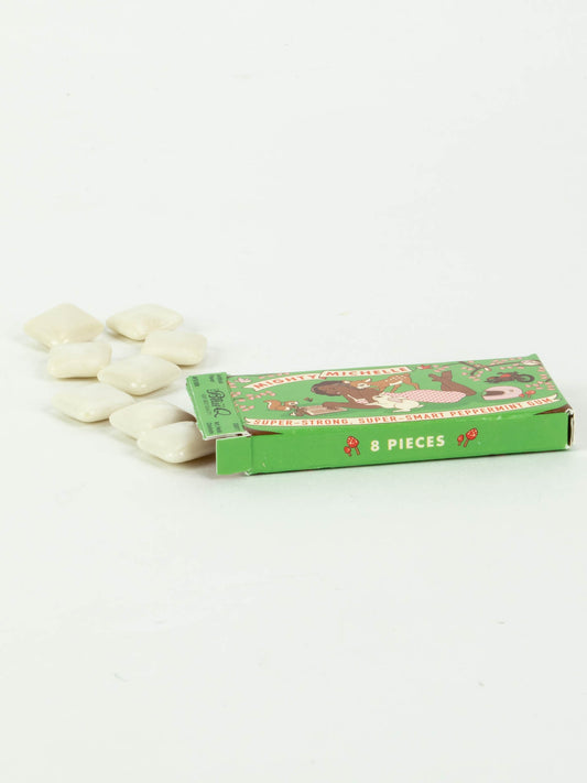 A green rectangular box labeled 8 PIECES contains seven white, square peppermint-like Mighty Michelle Gum pieces by Blue Q, partly slid out onto a white surface.