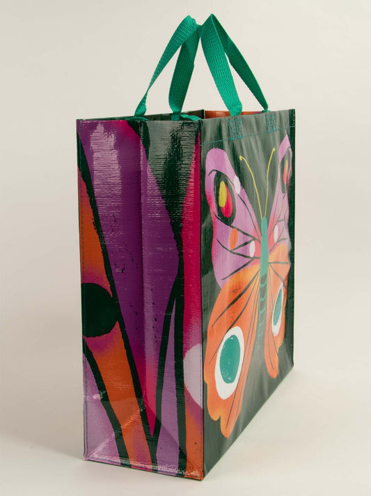 The Big Butterfly Shopper by Blue Q is a 6.2-gallon reusable tote with green handles and a vibrant butterfly design in orange, pink, and teal on a dark background—perfect for carrying your shopping essentials in style.