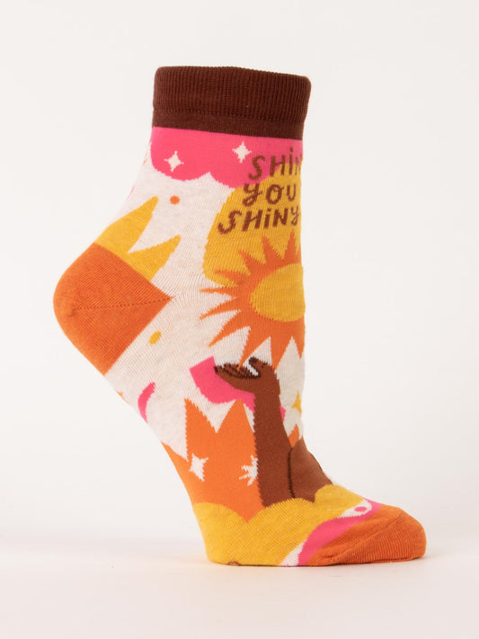 Blue Q Shine On You Crazy Shiny Thing W-Ankle Socks feature a colorful sun, orange rays, stars, and "Shine, you shiny" text. Made from a soft nylon/cotton blend with orange and brown accents. Stylish ankle-length design.