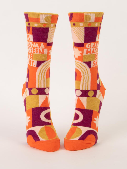 Blue Q’s "This Grandma Has Seen Some Shit" W-Crew Socks feature a bold geometric pattern in orange, yellow, purple, and white, made from combed cotton, nylon, and spandex—with the phrase printed across both socks.