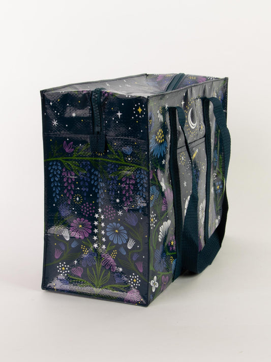 The Blue Q Starry Garden Shoulder Tote is a roomy rectangular bag with black handles, featuring a dark background adorned with colorful stars, crescent moons, and flowers in purple, white, and green.