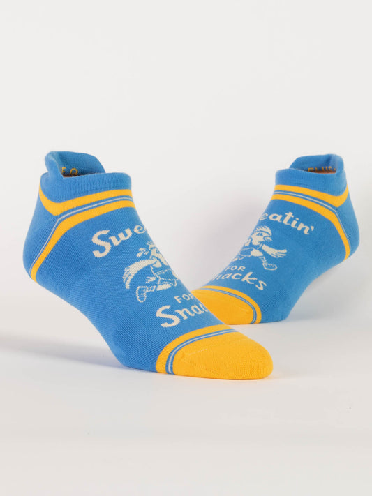 Blue Q Sweatin' For Snacks Sneaker Socks are blue ankle compression band socks with yellow toes and trim, white "Sweatin' For Snacks" text, and a running person graphic.