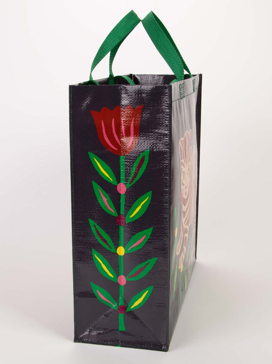 The Blue Q Tiger Kitten Shopper is a tall, rectangular reusable bag with sturdy green handles, showcasing a red and pink flower, green leaves, yellow accents, and soft whiskers on a dark background.