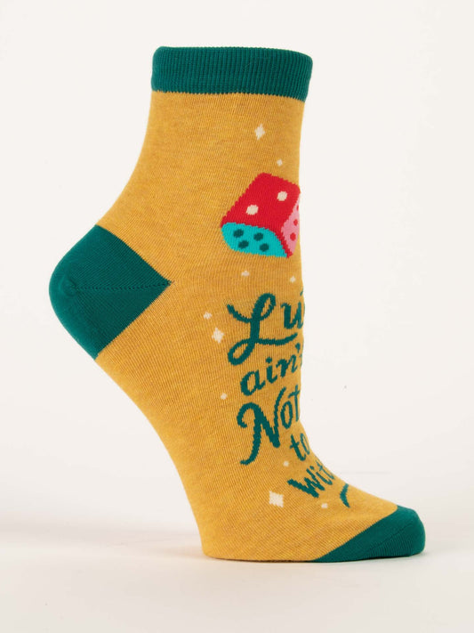 The Blue Q Luck Ain't Got Nothin' To Do With It W-Ankle Socks are yellow combed cotton with green toes, heel, and cuff, featuring two dice and the phrase in green text. Shown on a mannequin foot.