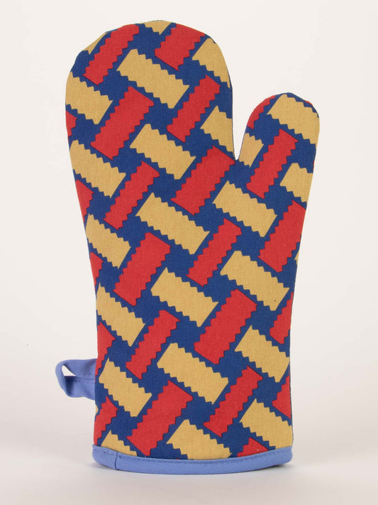 The Blue Q "Easy As Pie Is Such A Lie" Oven Mitt, featuring a geometric zigzag pattern in red, yellow, and dark blue, stands upright against a plain white background—perfect for your kitchen needs.