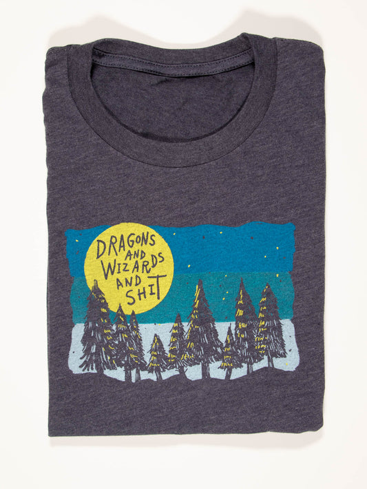 The Dragons And Wizards And Shit T-Shirt by Blue Q is a folded dark gray tee in soft Airlume combed cotton, featuring a forest at night with a yellow moon and the phrase screen-printed. Check unisex size chart for best fit.