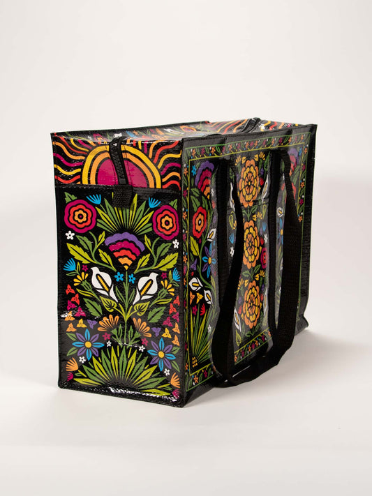 The Blue Q Flower Fest Shoulder Tote is a reusable shopping bag featuring black handles and vibrant nature-inspired patterns with flowers, leaves, and birds on a dark background.