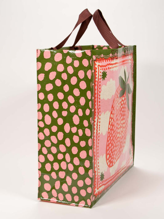 The Blue Q Strawberry Clouds Shopper is a rectangular reusable bag with brown handles, featuring a large Strawberry Clouds print on one side and an olive-green background with pink dots on the other sides.