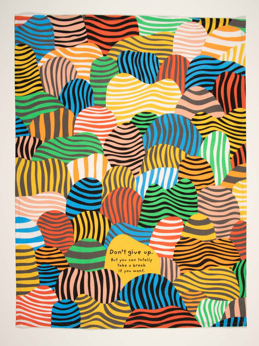 The Blue Q “Don't Give Up. But You Can Totally Take A Break If You Want.” dish towel features colorful overlapping shapes and wavy stripes, with inspiring text in the center—perfect for adding motivation to any kitchen.