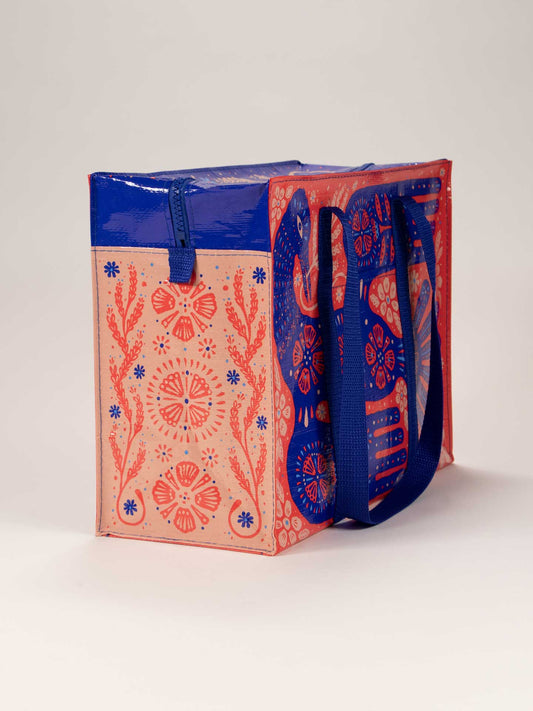 The Rare Bird Shoulder Tote by Blue Q features pink sides with red and blue floral and geometric patterns inspired by Stresemann's Bristlefront, plus a solid blue top, handles, and zipper.