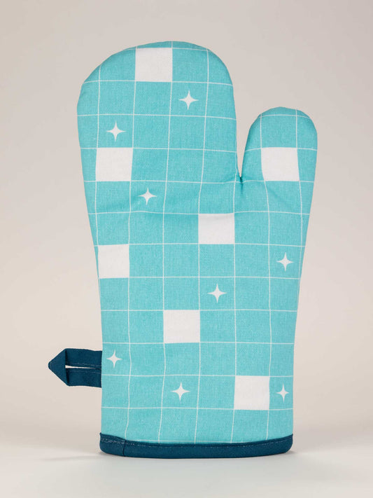 The Blue Q "Welcome To My Cooking Show!" Oven Mitt, featuring a turquoise color with a white grid and star pattern, stands upright against a plain light background.