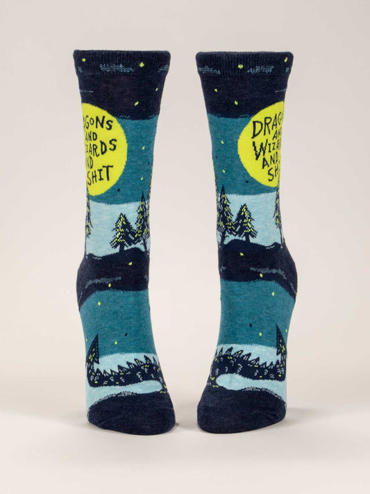 Blue Q's Dragons And Wizards And Shit W-Crew Socks feature a blue and navy night landscape with trees, a dragon, and a yellow moon displaying the phrase "Dragons and wizards and shit." Made of combed cotton.