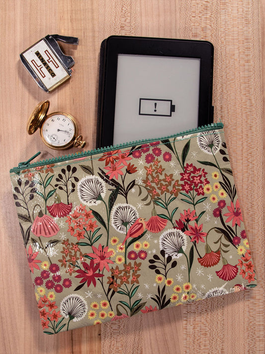 The Blue Q Dandelion Zipper Pouch, featuring a sage zipper, sits on wood holding an e-reader with low battery. Beside the pouch are an open pocket watch and a small retro alarm clock.