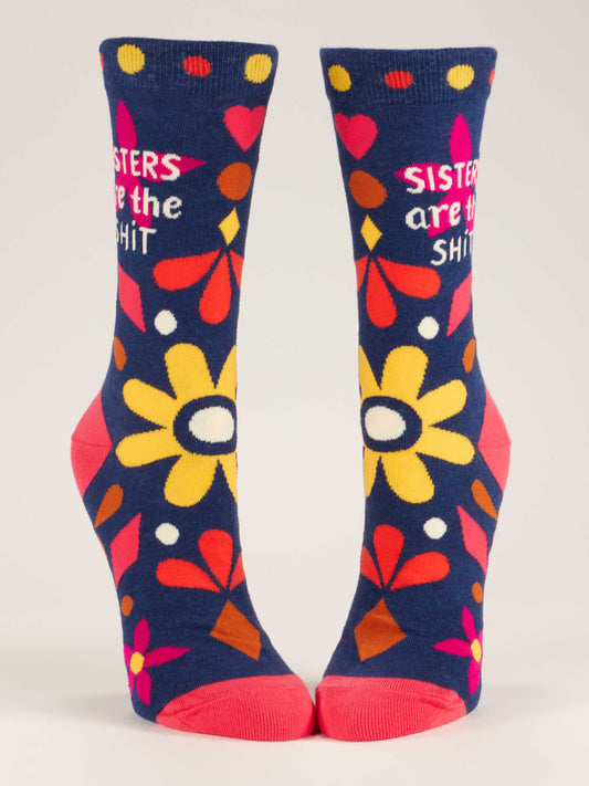 Blue Q Sisters Are The Shit W-Crew Socks: Blue novelty socks with colorful flowers, hearts, dots, and “SISTERS are the SHIT” in white and pink text. Pink heels and toes add extra charm to these fun family socks.