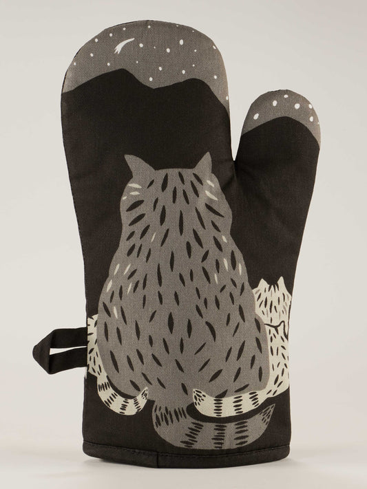 The Blue Q "Then Make Your Own Fucking Dinner" oven mitt is black with a gray and white cat gazing at a starry night sky, mountains, and crescent moon—wondering if there’s any trash to eat under the stars.