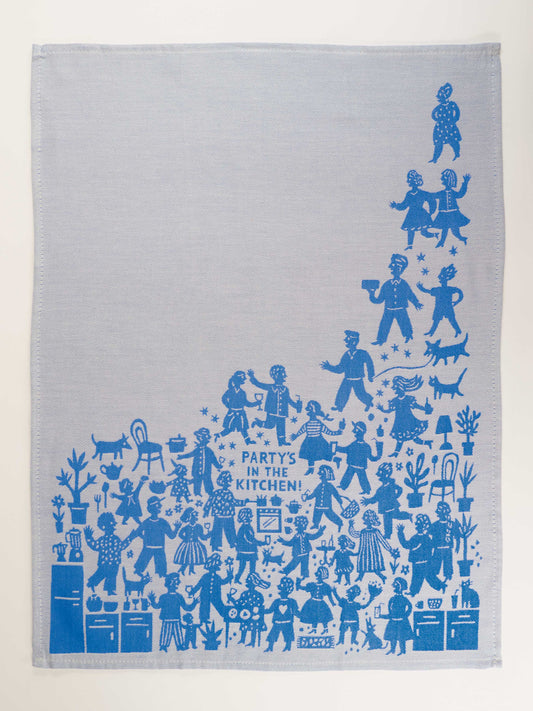 The "Party's In The Kitchen Dish Towel" by Blue Q is a light gray towel with a playful blue illustration of people, pets, and plants gathering in a kitchen, centered around the phrase “PARTY’S IN THE KITCHEN!”.