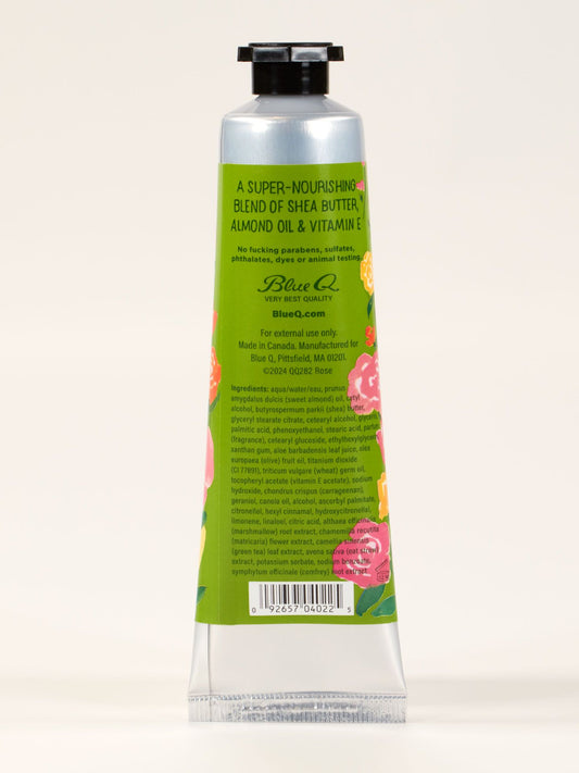 A green metal tube of Blue Q's "I'm A Delicate Fucking Flower Hand Cream – English Rose with Clover Elderflower," featuring floral designs and a nourishing blend of shea butter, almond oil, and vitamin E. Ingredients and usage listed on back.