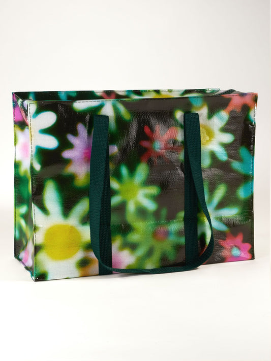 The Hazy Daisy Shoulder Tote by Blue Q is a large, rectangular bag with dark green handles and a vibrant, blurred floral pattern of white, yellow, and pink flowers on a dark background—both stylish and eye-catching.