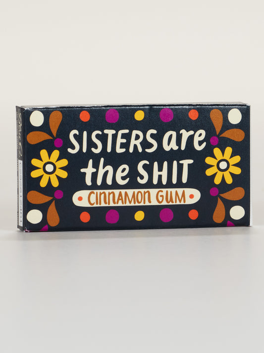 Blue Q Sisters Are The Shit Gum: A box of candy-coated cinnamon gum with colorful flowers and dots, bold white “Sisters Are The Shit” text, and 8 pieces per pack.