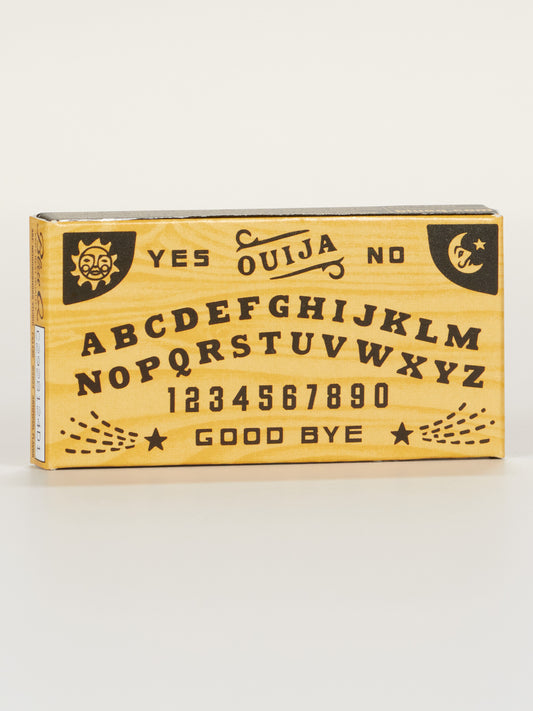 Blue Q’s Ouija Board Gum features a rectangular design with alphabet, numbers 0-9, YES, NO, GOOD BYE, sun and moon symbols on a wood-like background—perfect for spirit communication sessions.