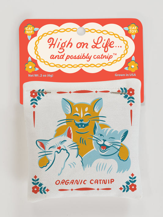 A Blue Q High On Life...And Possibly Catnip Toy package features three illustrated happy cats and highlights Organic Catnip, Grown in USA. The packaging also promotes healthy play with each irresistible catnip inside.